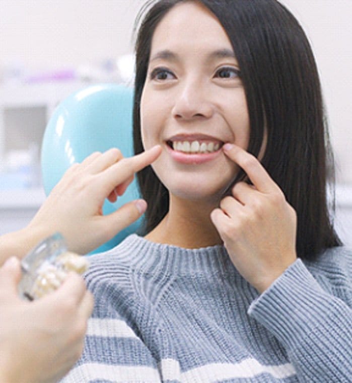 A young female pointing to her teeth while a dentist also points to an area in which a dental implant in Greenwood would be beneficial