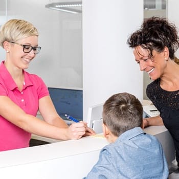 A dental receptionist explaining the cost of dental implant treatment with a mom and her two children