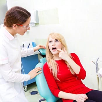 A female patient pointing to a problem tooth while the dentist listens to her problem