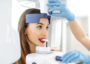 A woman standing at the Conebeam/CT 3D scanner while a dental assistant assists