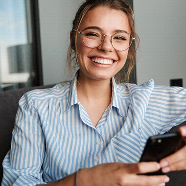 woman smiling with glasses and holding her phone 