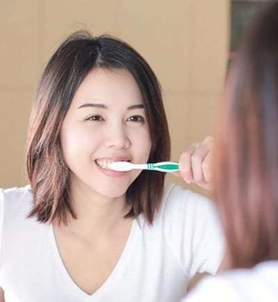 Woman looking in the mirror while brushing her teeth