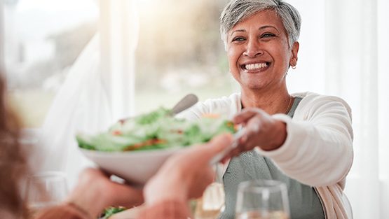 Smiling woman grabbing salad bowl across the table