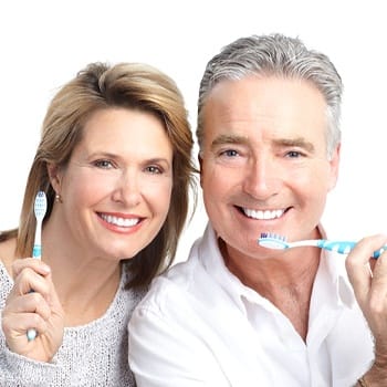 Older couple smiling and holding toothbrushes.