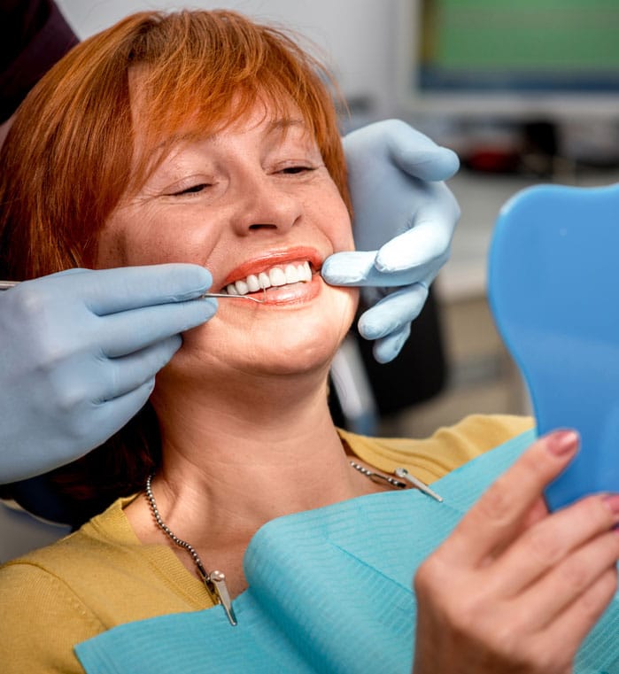 Woman in dental chair looking at new denture in mirror