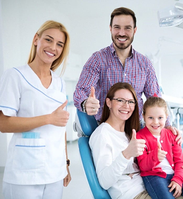 A husband, wife, and young daughter giving a thumbs up next to their family dentist in Greenwood, SC