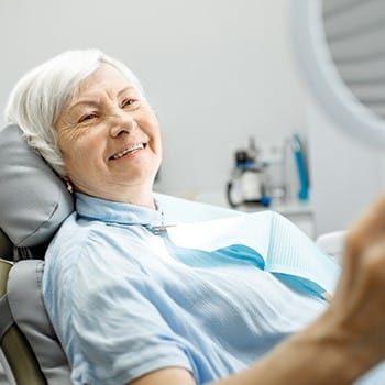 patient with dental implants in Greenwood admiring her new smile in the mirror 
