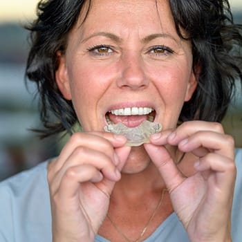 A woman inserts a mouthguard to protect her dental implants in Simpsonville