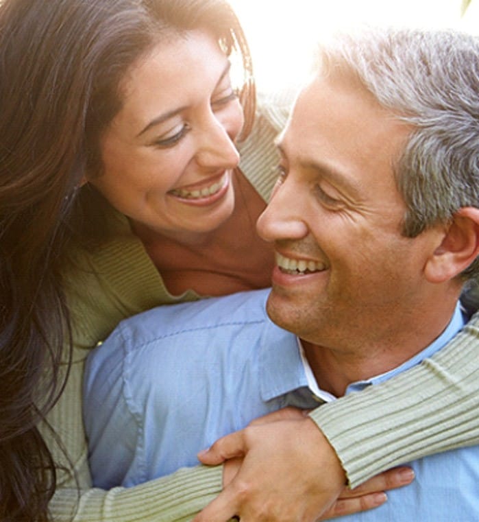 A middle-aged couple smiling and hugging each other after seeing their dentist in Greenwood for restorative treatment