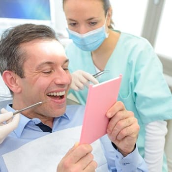A middle-aged man looking at his smile in the mirror after receiving his custom-made dental crown