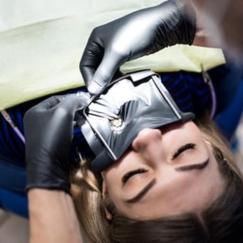 A dentist using a dental dam to isolate a woman’s tooth in preparation for root canal therapy
