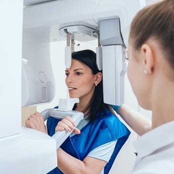 A woman standing at the Conebeam/CT 3D scanner while a dental assistant observes