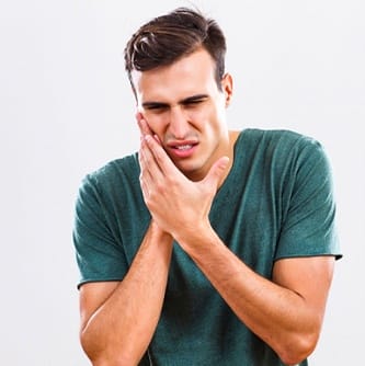 man in green shirt holding mouth in pain 