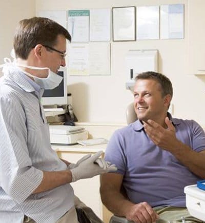 Man in dental chair talking to dentist about TMJ dysfunction