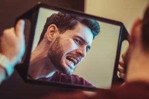 person inspecting cosmetic dental flaws in a mirror