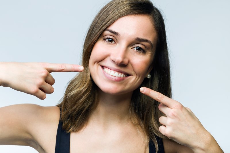 young woman smiling and pointing to her white teeth