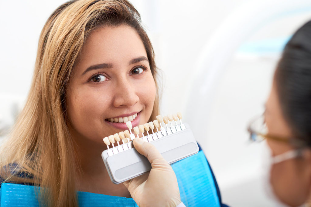 dentist holding veneers up to a patient’s teeth 