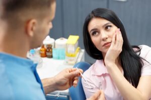 Patient in dentist’s chair holding her mouth and looking at dentist.